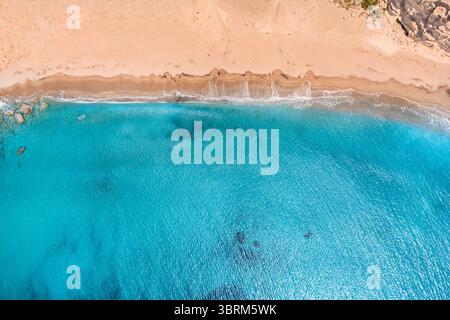 Vue aérienne de l'eau turquoise lavant doucement le sable doré sur une plage ensoleillée créant une atmosphère estivale relaxante Banque D'Images