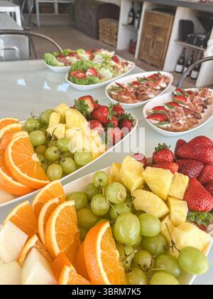 Plateau de fruits frais avec des oranges, des raisins, des fraises et des ananas disposés magnifiquement sur une table, favorisant une alimentation saine et dynamique Banque D'Images