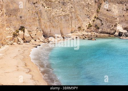 Une eau turquoise cristalline se dégageant doucement contre une plage de sable isolée nichée sous d'imposantes falaises blanches Banque D'Images