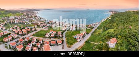 Drone capturant un coucher de soleil à couper le souffle sur une charmante ville côtière avec des maisons aux toits rouges, des champs verdoyants et des eaux bleues calmes Banque D'Images