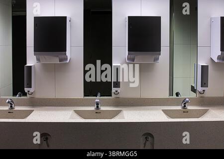 Intérieur d'une salle de bain publique moderne avec plusieurs éviers avec robinets automatiques chromés, miroirs, distributeurs de savon et de serviettes. Banque D'Images