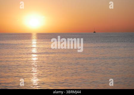 Coucher de soleil vif sur la mer avec un soleil brillant et un reflet doré sur l'eau calme. Atmosphère paisible et captivante. Fond de nature, relaxati Banque D'Images