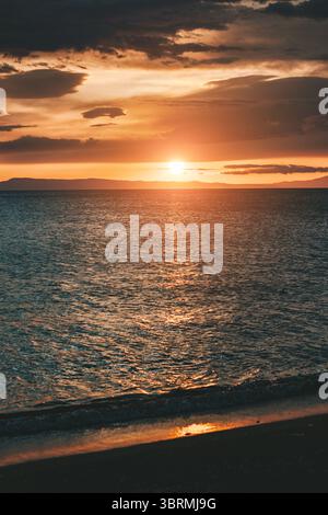 Coucher de soleil sur les eaux calmes de l'océan, projetant une lumière dorée chaude et créant une atmosphère sereine Banque D'Images