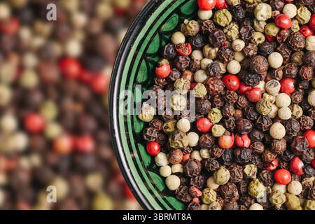 Mélanger les grains de poivre dans un bol vert. Épices de poivre blanc noir rouge. Assaisonnement aromatique en gros plan. Mélange d'épices coloré pour la cuisson. Banque D'Images