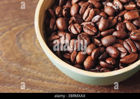 Faire dorer les grains de café torréfiés. Bol en bambou sur fond en bois. Ingrédient aromatique de boisson à base de caféine. Concept énergie et matin. Grains de tir macro. Banque D'Images