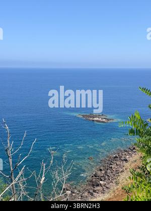 Vue imprenable sur l'océan depuis une falaise, mettant en évidence les eaux bleues profondes et le ciel clair. La côte rocheuse et la végétation clairsemée s'ajoutent à Banque D'Images
