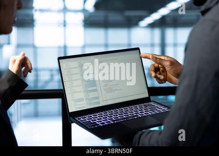 Développeurs de logiciels dans le centre de données utilisant un ordinateur portable, employant des modèles d'apprentissage automatique. Gros plan sur les employés qui utilisent des ordinateurs portables pour répondre aux besoins de l'infrastructure et allouer les ressources de manière efficace Banque D'Images