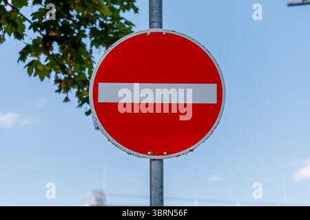 Gros plan d'un panneau allemand rouge et blanc « ne pas entrer » monté sur un poteau métallique contre un ciel bleu, avec des feuilles d'arbre visibles. Banque D'Images