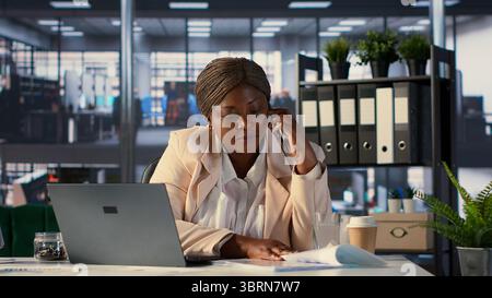 Une entrepreneure afro-américaine travaille sur la planification financière sur son téléphone portable, répondant à un appel des investisseurs pour partager des idées et des données. Femme PDG fait des tâches commerciales sur appel téléphonique. Caméra A. Banque D'Images