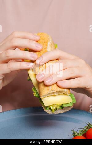 Gros plan des mains tenant sandwich baguette avec fromage et laitue au-dessus de l'assiette, prêt à manger, collation rapide, mode de vie manger Banque D'Images