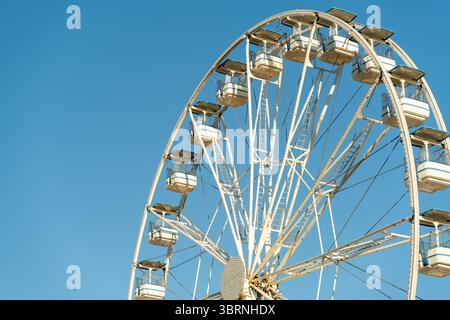 Grande roue se dresse contre un ciel bleu vif, mettant en valeur sa structure blanche et ses gondoles. Banque D'Images