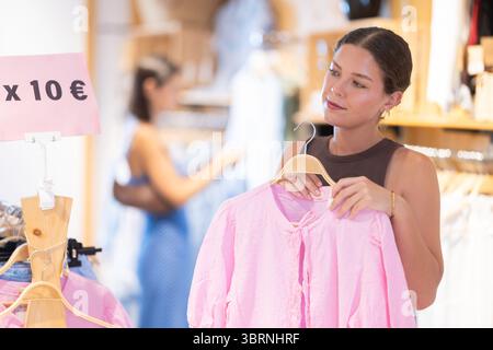 La cliente fille choisit chemisier dans le magasin, et l'acheteur examine soigneusement le produit. Banque D'Images