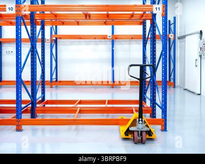 Transpalette à main jaune ou transpalette hydraulique, garé près du rack, étagères en acier, prêt à charger des marchandises, dans l'entrepôt. Levage manuel. Bac à palettes Banque D'Images
