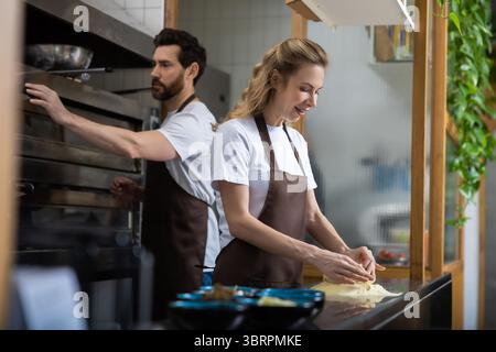 Boulangers masculins et féminins travaillant ensemble dans une cuisine de boulangerie, discutant des ingrédients sur un comptoir Banque D'Images
