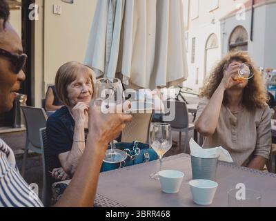 Trois amies mûres de diverses ethnies se réunissant dans un café en plein air, prenant un verre et s'engageant dans une conversation animée, créent un cheerfu Banque D'Images