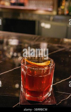 Gros plan d'un cocktail Negroni classique servi dans un verre à facettes avec une touche de zeste d'orange. La boisson se trouve sur un comptoir de bar en marbre Banque D'Images