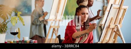 Jeune femme caucasienne adulte se concentrant tout en peignant sur toile dans Studio Banque D'Images