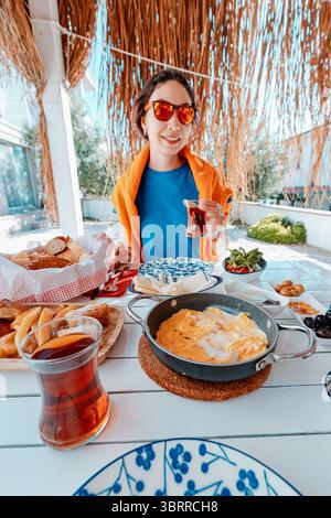Touriste ayant un délicieux petit déjeuner turc avec thé, omelette, viennoiseries, fromage, olives, salade et autres spécialités locales Banque D'Images