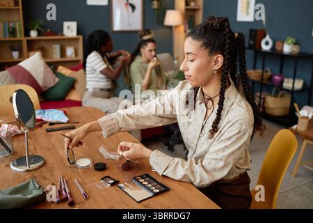 Femme multiculturelle appliquant le maquillage à la table avec des amis parlant Banque D'Images
