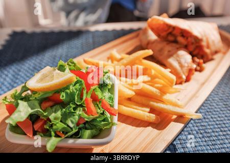 Délicieux wrap de poulet servi avec des frites croustillantes et une salade fraîche sur un plateau en bois, parfait pour un repas satisfaisant Banque D'Images