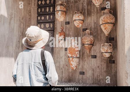 5 mai 2025, Canakkale, Turkiye : touriste admirant d'anciennes amphores accrochées à un mur de béton dans un musée d'archéologie Banque D'Images