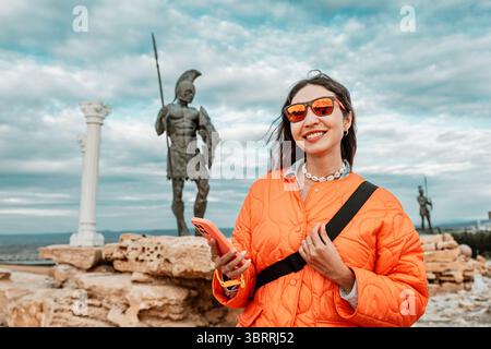 05 mai 2025, Uluova, Turkiye : femme touriste avec smartphone près de la statue guerrière d'inspiration Iliade près des ruines de Troie Banque D'Images