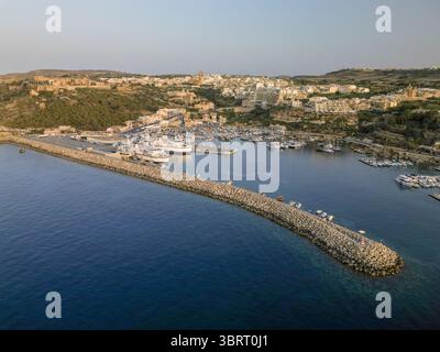 Vue aérienne du brise-lames embrassant le port, où les bateaux reposent sous le regard attentif de l'ancienne citadelle, Gozo, Malte. Banque D'Images