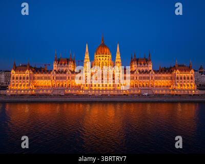 Vue aérienne du bâtiment illuminé du Parlement hongrois réfléchissant sur le paisible Danube sous un ciel crépusculaire, Budapest, Hongrie. Banque D'Images