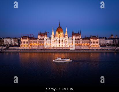 Vue aérienne du bâtiment illuminé du Parlement hongrois reflété dans les eaux tranquilles du Danube, son architecture ornée brille sur le ciel crépusculaire, Budapest, Hongrie. Banque D'Images