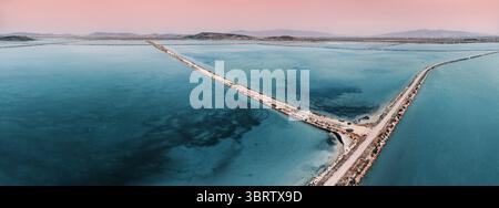 Vue aérienne des étangs d'évaporation de sel créant une belle surface d'eau turquoise divisée par des routes au coucher du soleil Banque D'Images