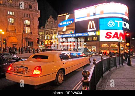 Limousine de luxe extensible dans le West End de Londres transportant des passagers en visite dans la circulation nocturne hivernale très fréquentée en circulant autour du célèbre carrefour routier Piccadilly Circus et du lieu de rassemblement populaire dominé par des panneaux publicitaires lumineux éclectiques en couleur dans la ville de Westminster Londres Angleterre Royaume-Uni image nocturne de l'année 2000. Banque D'Images