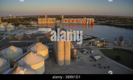 Vue aérienne de l'ascenseur de grain ADM Toledo orné d'une fresque murale vibrante de tournesol le long de la rivière Maumee reflétant la lueur du coucher du soleil, Toledo, Ohio, États-Unis. Banque D'Images