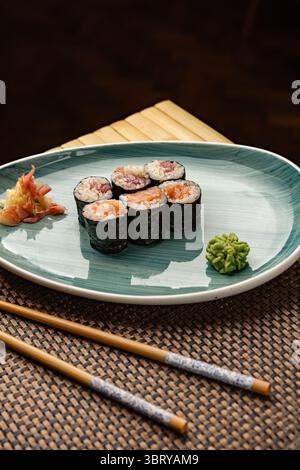 Rouleaux de hosomaki frais, remplis de saumon et de thon, servis avec du gingembre mariné et du wasabi, présentés sur une assiette élégante avec des baguettes à proximité Banque D'Images