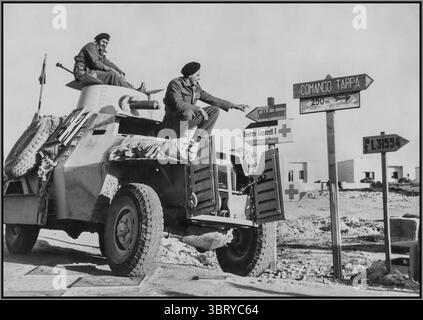 Seconde Guerre mondiale en Afrique du Nord, représentant les troupes alliées dans un véhicule blindé tentant de lire les panneaux routiers allemands et italiens dans Derna, en Libye. La voiture blindée semble être un modèle britannique, probablement un Humber ou un Marmon-Herrington , couramment utilisé par les forces alliées dans les campagnes du désert. Les soldats font probablement partie d'une unité de reconnaissance ou de patrouille britannique, naviguant sur un territoire capturé inconnu indiqué par les panneaux en langue étrangère. Afrique du Nord 1943 Banque D'Images
