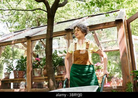 Femme âgée joyeuse jouit de la sérénité dans son jardin, entourée de plantes et d'arbres en fleurs. Banque D'Images