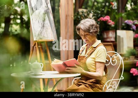Dans un jardin animé, une femme âgée lit paisiblement parmi les fleurs. Banque D'Images