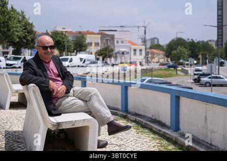 Vieil homme espagnol dans un blazer assis sur un banc dans une petite ville portugaise, regardant la plage Banque D'Images