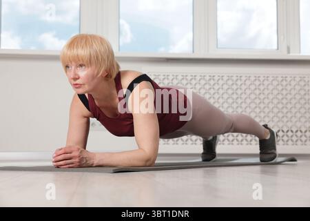 Femme senior dans les vêtements de sport faisant de l'exercice de planche à la maison Banque D'Images