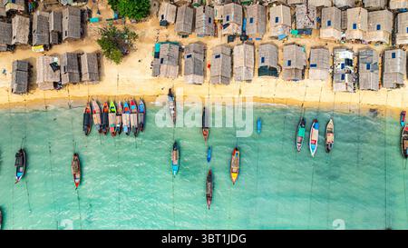 Une vue aérienne imprenable sur un village balnéaire tropical avec des rangées de petites cabanes le long du littoral, les bateaux de pêche traditionnels sont ancrés dans le turquois Banque D'Images