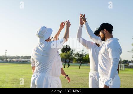 Divers coéquipiers masculins de cricket se sont élevés sur un terrain d'herbe ensoleillé portant des uniformes de cricket blancs Banque D'Images