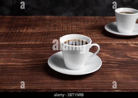 Deux tasses blanches de café noir reposent sur une riche table en bois brun. Banque D'Images