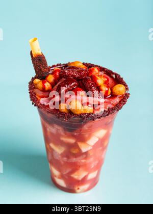 Petit verre fou, un mélange d'ingrédients sucrés, salés et épicés isolé sur fond bleu. Snack typique du Mexique. Banque D'Images