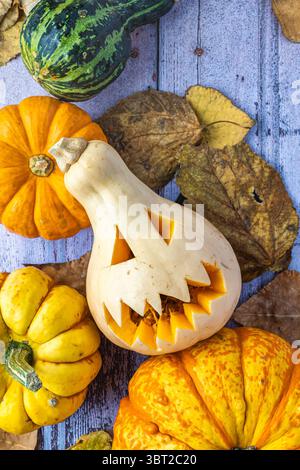 image zénithal avec citrouille effrayante sculptée, feuilles et petites citrouilles, fond en bois antique, ton festif et automnal. Banque D'Images