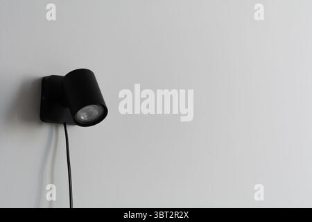 Projecteur mural noir moderne avec tête réglable sur un mur gris minimaliste. Banque D'Images