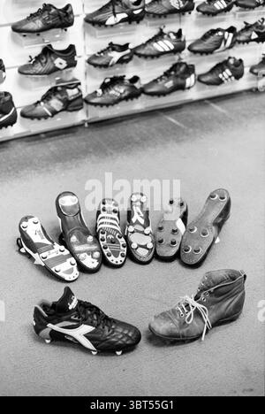 Chaussures de football, Whizgle News, Dutch Desk, pays-Bas, 1950 - 2000 le 16-08-1993. Ces rubriques sont illustrées dans l'image. La scène présente une collection de chaussures variées, principalement axées sur les crampons de football (soccer). Dispersées sur un sol texturé, plusieurs paires de crampons noirs présentent différents styles et designs. Les chaussures semblent avoir des niveaux d'usure variables, certaines semblant neuves tandis que d'autres montrent des signes d'utilisation. Parmi les crampons, il y a une paire distincte qui se distingue par ses couleurs vibrantes, éventuellement accentuées de teintes blanches ou rouges, contrastant avec la predom Banque D'Images
