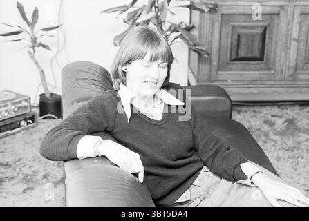 Portrait MRS Teelen ter Worm 70 Schalkwijk Portraits, Whizgle News, Dutch Desk, pays-Bas, 1950 - 2000 on 24-10-1977. Voici les rubriques de l'image. La scène montre une femme assise confortablement sur un canapé en cuir foncé. Elle a une coupe de cheveux bob courte et porte un pull foncé sur une chemise à col, créant un look décontracté mais poli. Son expression est détendue, les yeux doucement fermés et un léger sourire, suggérant un moment de contentement ou de réflexion. Autour d'elle, le cadre est confortable et accueillant. Le canapé est positionné dans un espace de vie bien meublé décoré avec un couple de Banque D'Images