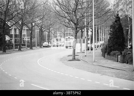 Aperçu César Francklaan Heemstede Straten Heemstede César Francklaan pays-Bas, Whizgle News, Dutch Desk, pays-Bas, 1950 - 2000 sur 06-01-1976. L'image montre ces rubriques. La scène présente une route sinueuse qui courbe doucement, accompagnée d'une palette douce et discrète dominée par des nuances de gris. De chaque côté, des arbres arides se dressent hauts, leurs branches dépourvues de feuilles, créant une apparence quelque peu brutale contre le ciel couvert. L'atmosphère est tranquille et tamisée, évoquant un sentiment de calme, peut-être une allusion au début du printemps ou à la fin de l'automne. Sur le côté gauche, un groupe de résidentes Banque D'Images