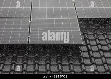 Bord inférieur de l'installation de panneau solaire avec des tuiles de toit sombres et de fortes pluies. Banque D'Images