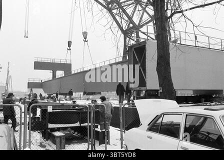 Grue de chargement à Figee Figee Haarlem pays-Bas, Whizgle News, Dutch Desk, pays-Bas, 1950 - 2000 le 19-02-1979. Ce sont les éléments de l'image. La scène représente un chantier de construction très fréquenté dans une atmosphère hivernale. Le ciel est couvert, projetant une lumière grise et terne sur la zone, ce qui améliore la sensation de froid et industrielle. Le sol est recouvert d'une fine couche de neige, et les travailleurs sont revêtus de lourds vêtements d'hiver pour se protéger contre le froid. Au premier plan, il y a plusieurs personnes engagées dans diverses tâches. Certains sont axés sur la gestion de l'équipement, tandis que d'autres sont discutés Banque D'Images