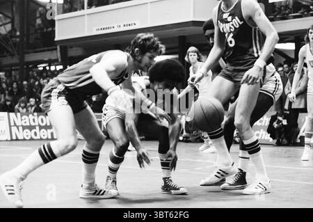 Match de basket Levi's Flamingos - Transol dans la salle de sport Kennemer Haarlem pays-Bas, Whizgle News, Dutch Desk, pays-Bas, 1950 - 2000 en 1974. Ces rubriques sont illustrées dans l'image. La scène capture un moment dynamique dans un match de basket-ball, avec des joueurs intensément engagés dans l'action. Deux athlètes sont bien en vue au premier plan, l'un plongeant vers un basket-ball lâche, mettant en valeur l'effort et la détermination. Le short foncé et le maillot rayé du joueur contrastent avec le blanc éclatant de l'uniforme de l'adversaire, créant une tension visuelle convaincante. Autour d'eux, le réglage est rempli d'esprit Banque D'Images